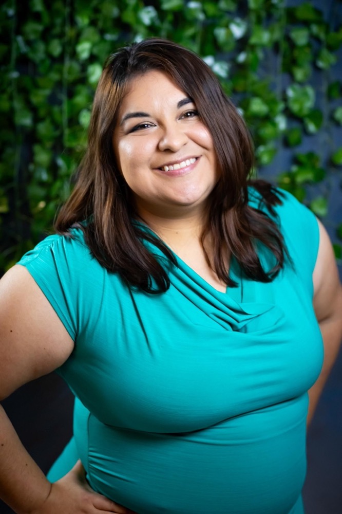 Desiree Carscadden, Community & Events Director at Holistic Healers Community in Upland, California, smiling in a teal top with leafy green background.